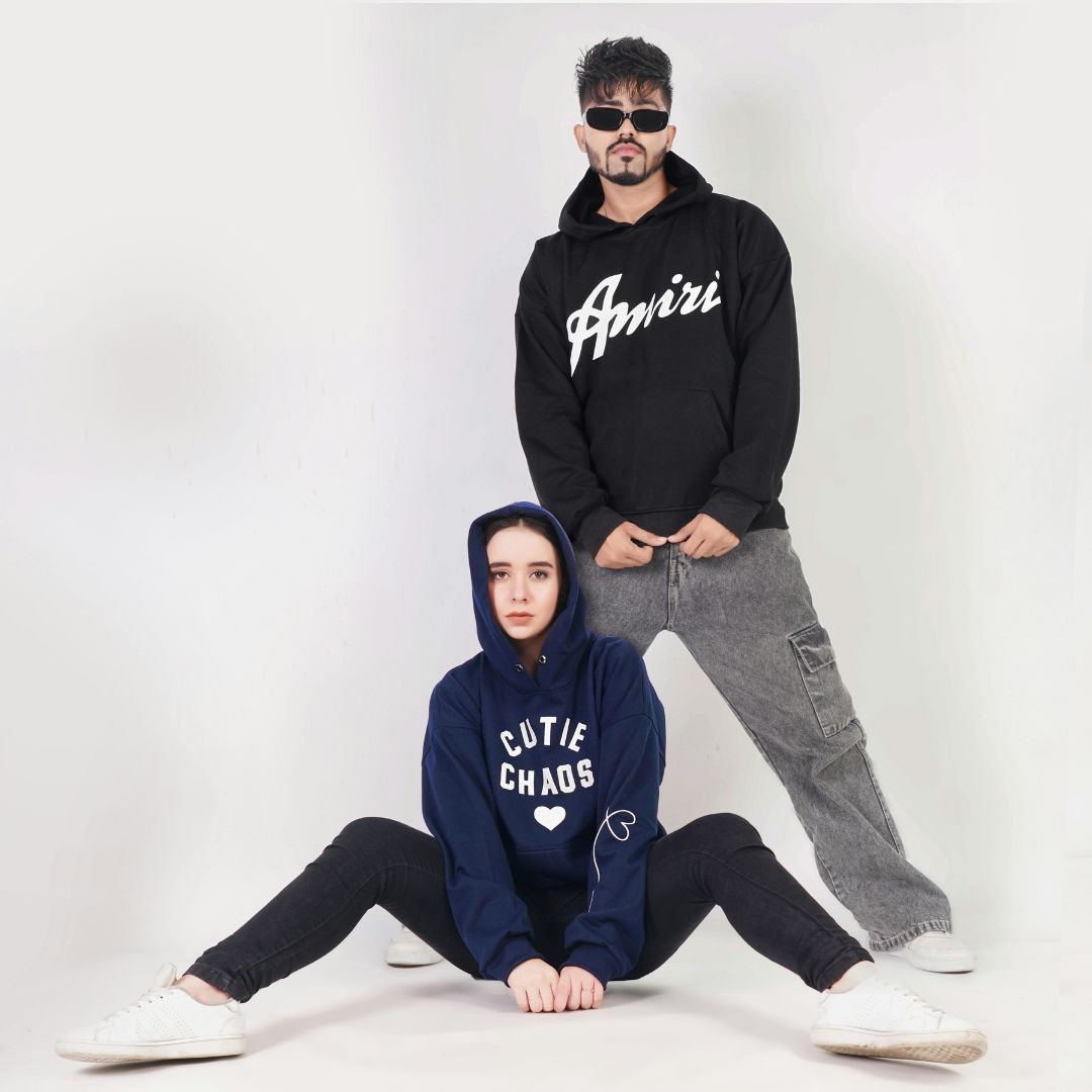 Two models wearing dark graphic hoodies in a studio.