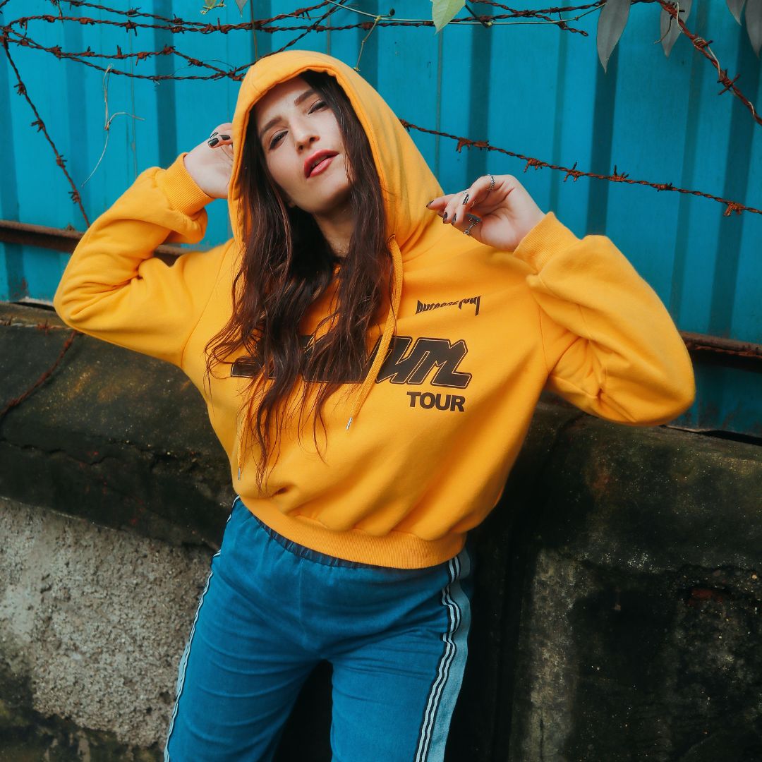 Model smiling outdoors in a bright orange hoodie.