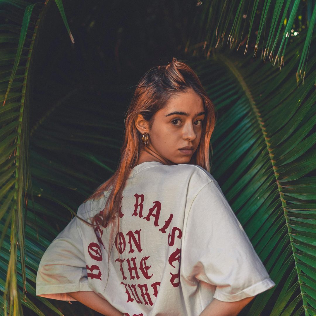 Cream oversized T-shirt worn in front of tropical leaves.